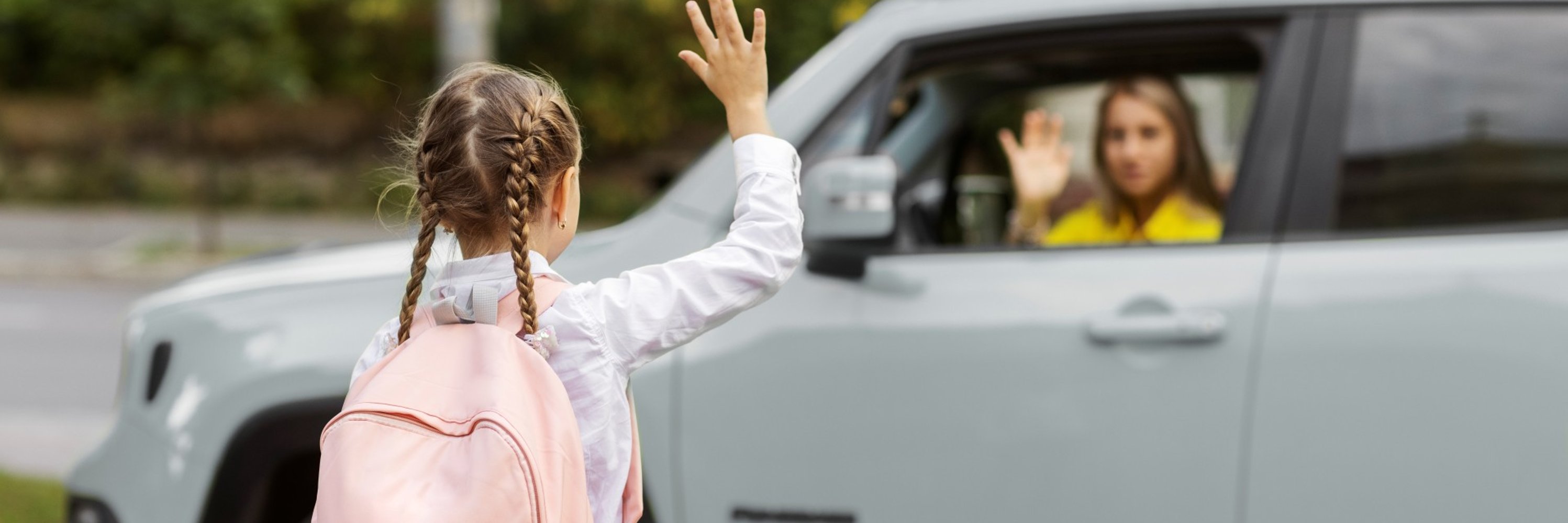 Schulkind winkt Mutter im Auto