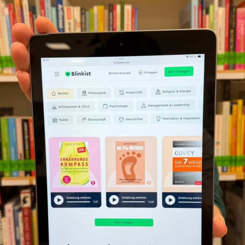 Im Vordergrund ist auf einem Tablet die Website von Blinkist zu sehen. Diese fasst Bücher in höchstens 20 min. auf Ihren Inhalt zusammen. Im Hintergrund ist die Bibliothek mit Bücher zu sehen.