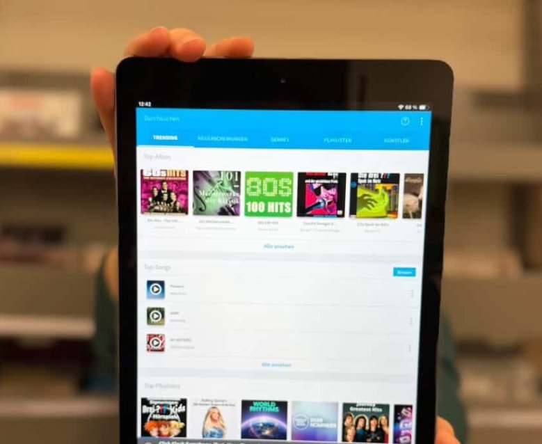 Im Vordergrund ist auf einem Tablet die App von Freegalmusic zu sehen. Mit dieser kann man Musik oder Hörspiele kostenfrei hören. Im Hintergrund ist die Bibliothek mit CDs zu sehen.