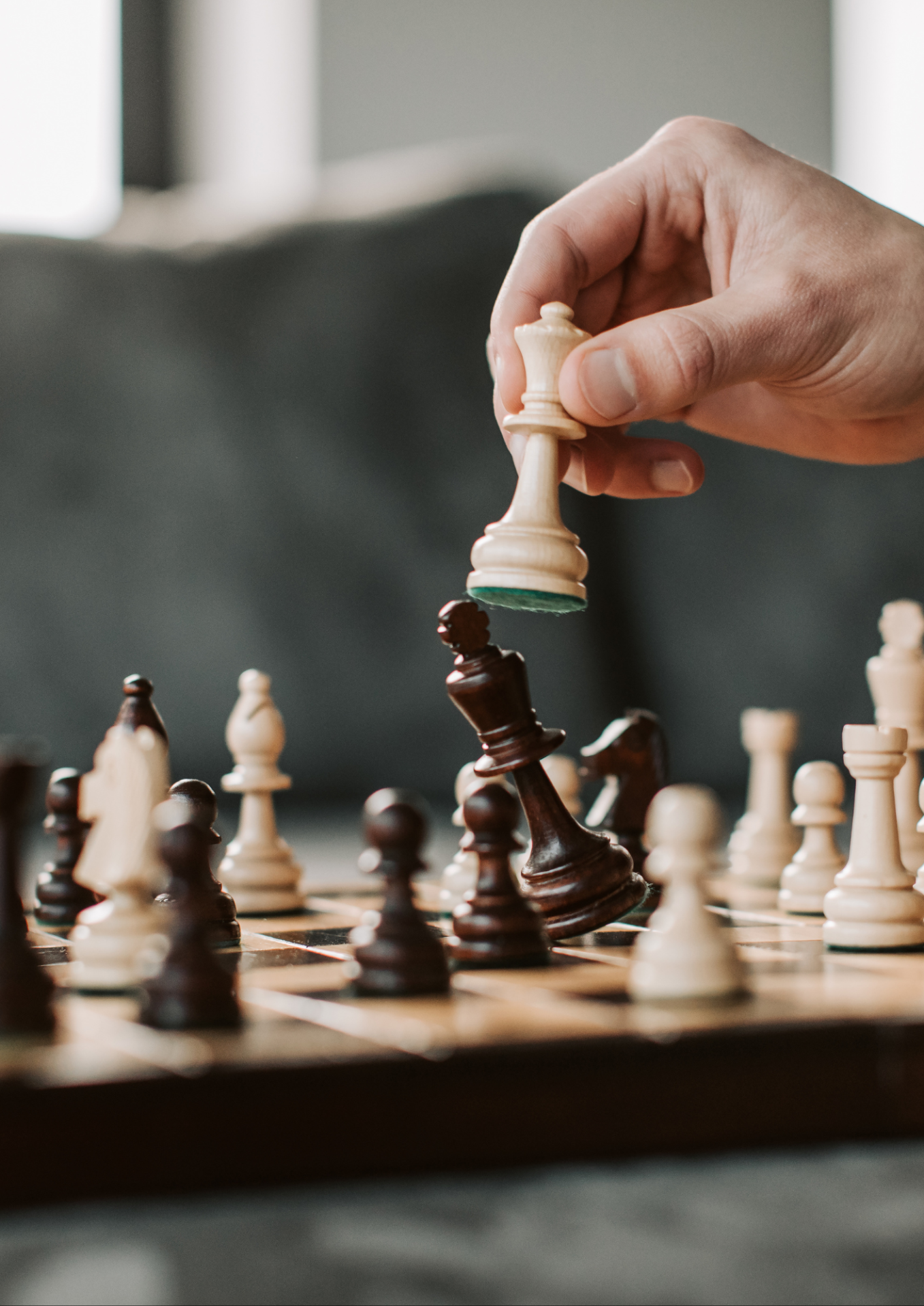 Zu sehen ist ein Schachbrett mit Schachfiguren die von einer Hand bewegt werden.