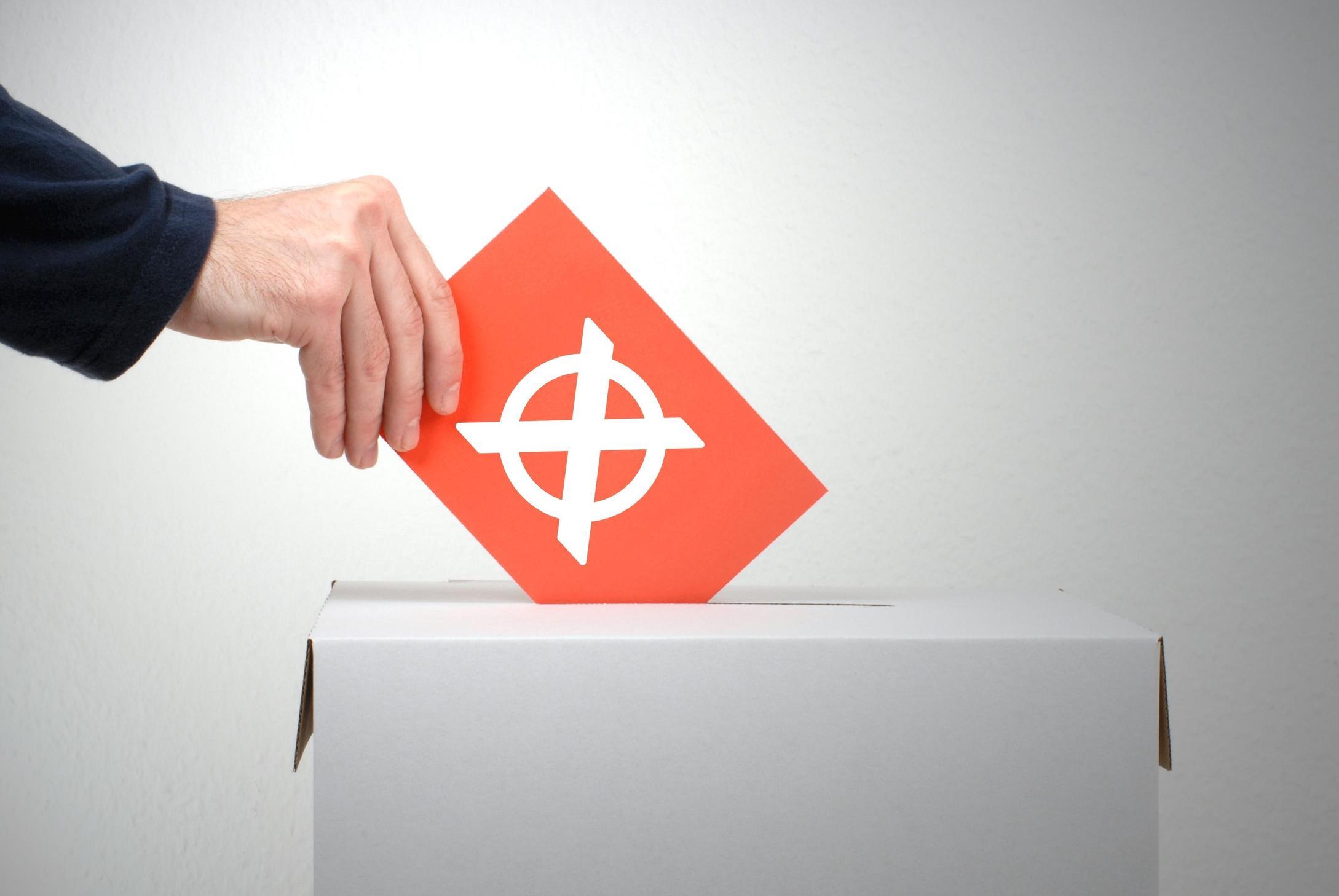 Wahlzettel mit großem Kreuz wird in eine Urne geworfen