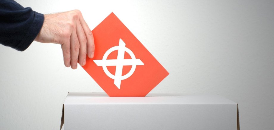Wahlzettel mit großem Kreuz wird in eine Urne geworfen