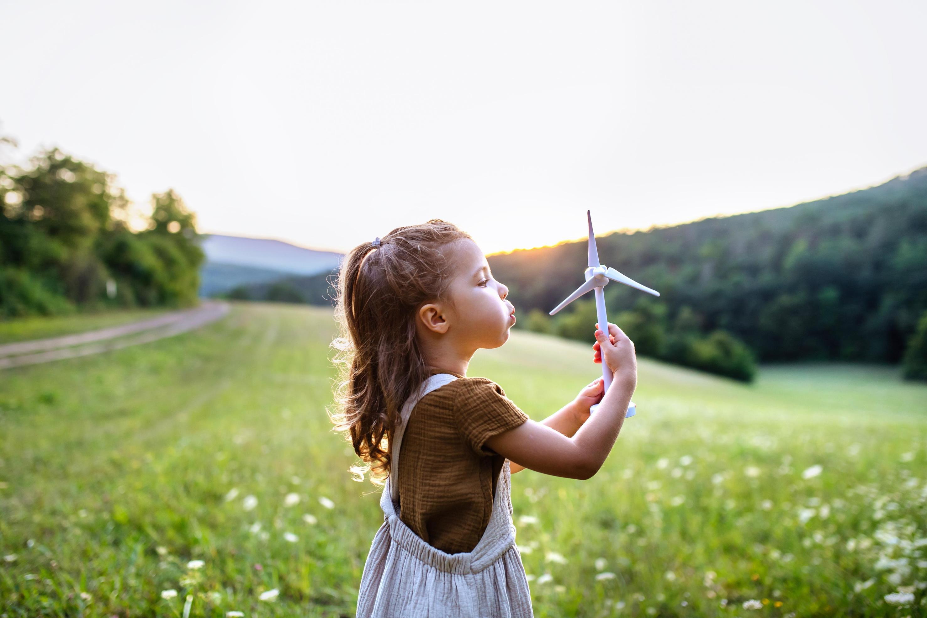 Little girl standing in nature with model of wind turbine. Concept of ecology future and renewable resources.