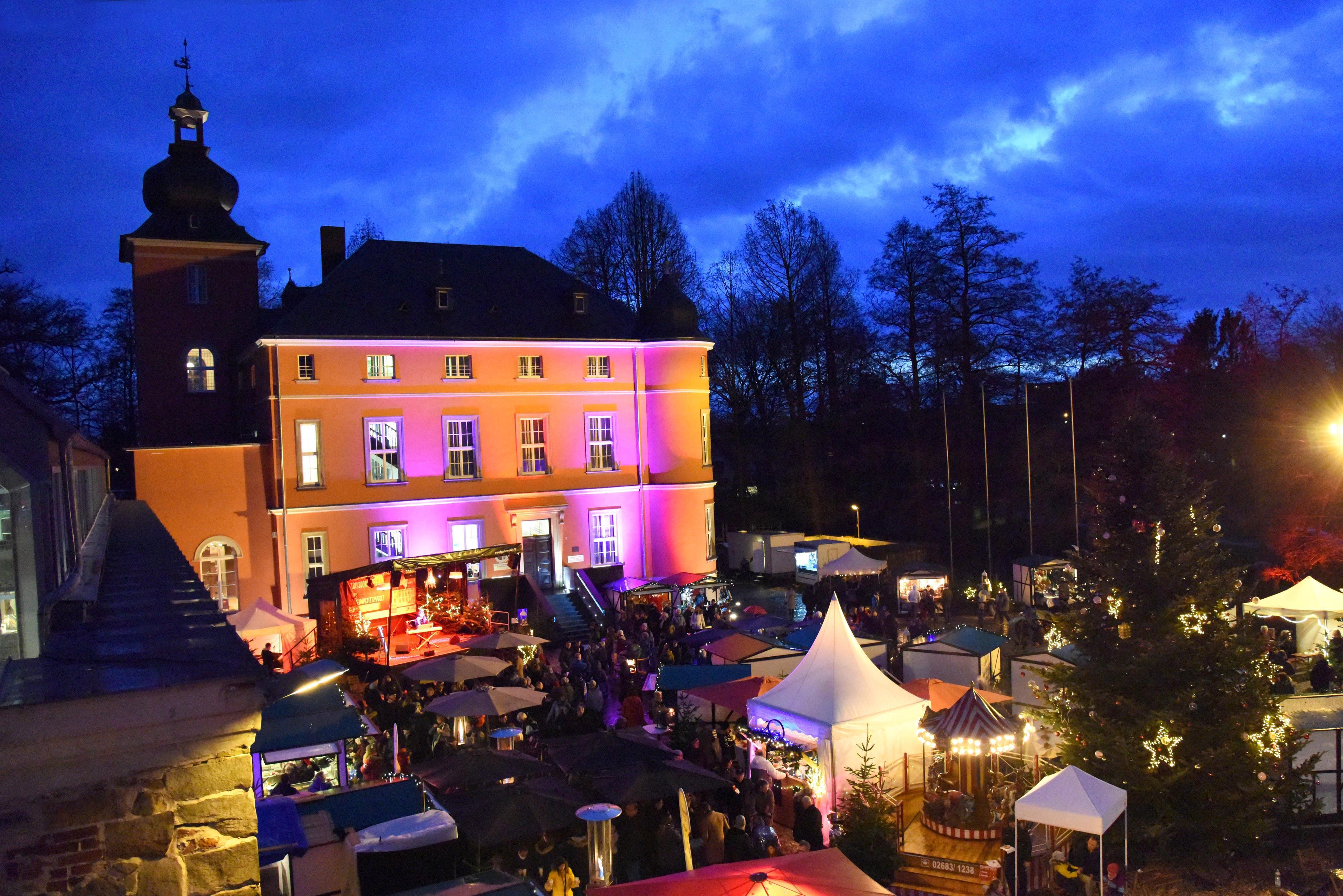 Zu sehen ist die mit bunten Farben, beleuchtete Burg Wissem während des Weihnachtsmarktes