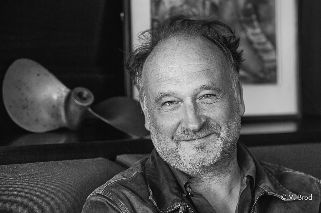 Jörg Bong auf einer Couch, schwarz-weiß Portrait, im Hintergrund eine Schiffsschraube und ein gerahmtes Bild