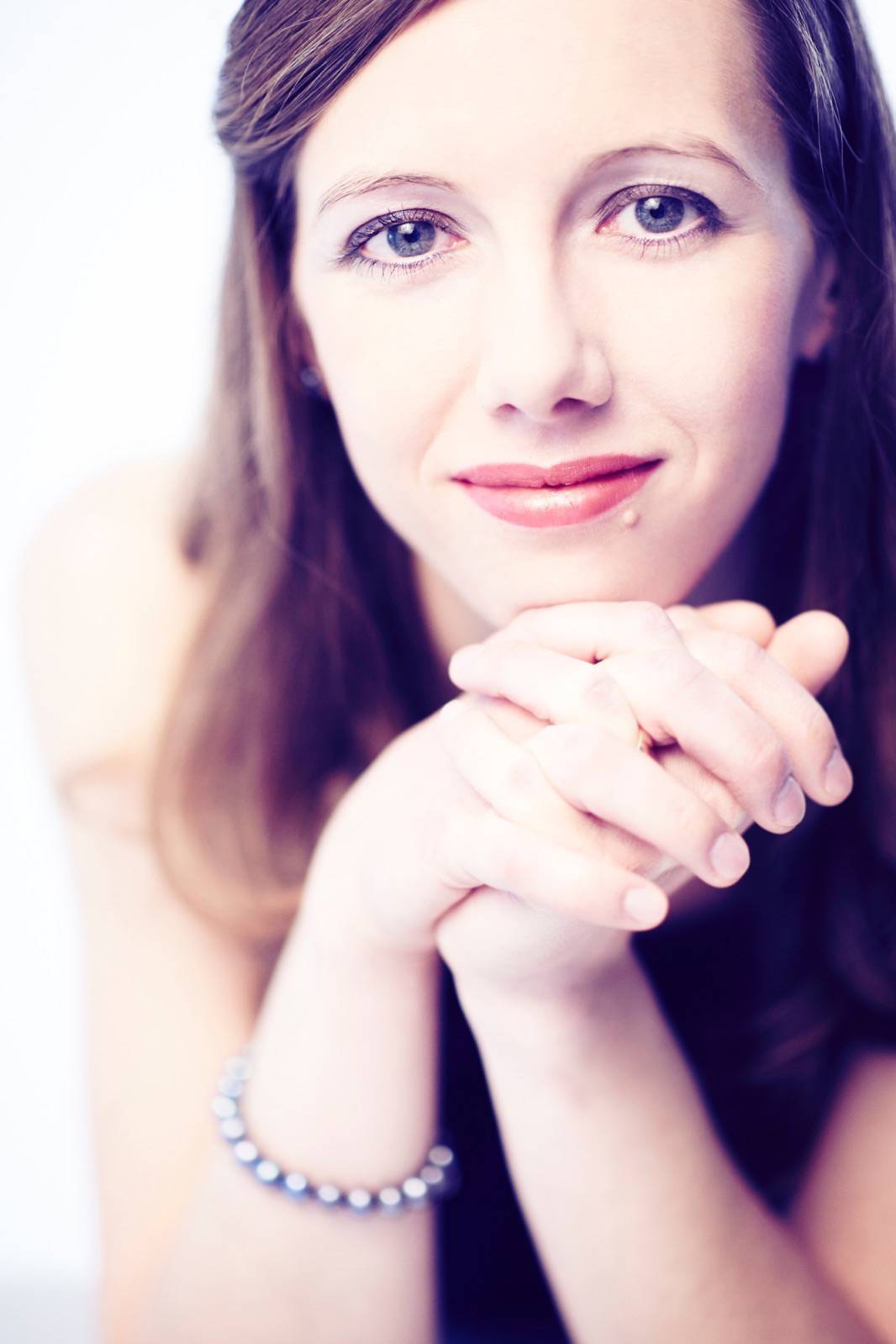 Elvira Bill; braunes langes Har, blaue Augen, lächelt, trägt eine silberne Armkette aus Kugeln, Portrait mit Tiefenunschärfe