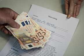 Eine männliche Hand hält mehrere 50 Euro-Scheine, eine weibliche Hand einen Mietvertrag.