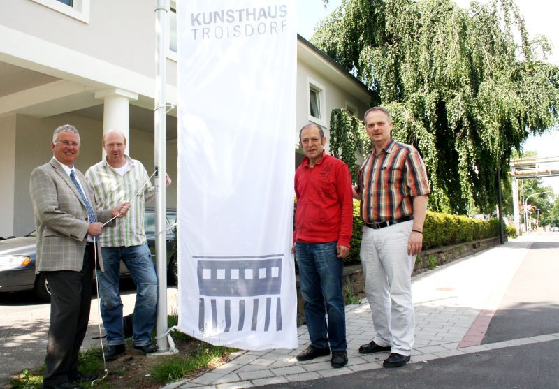 Eine neue Fahne mit dem Emblem des Kunsthauses Troisdorf hißte Bürgermeister Klaus-Werner Jablonski vor dem Gebäude, das als städtische Galerie im Herbst letzten Jahres eröffnet worden war. Die Fahne weht jetzt pünktlich zur Eröffnung der nächsten Ausstellung: