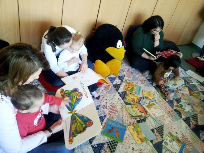 Troisdorfer Kleinkinder wälzen zusammen mit ihren vorlesenden Müttern Bilderbücher