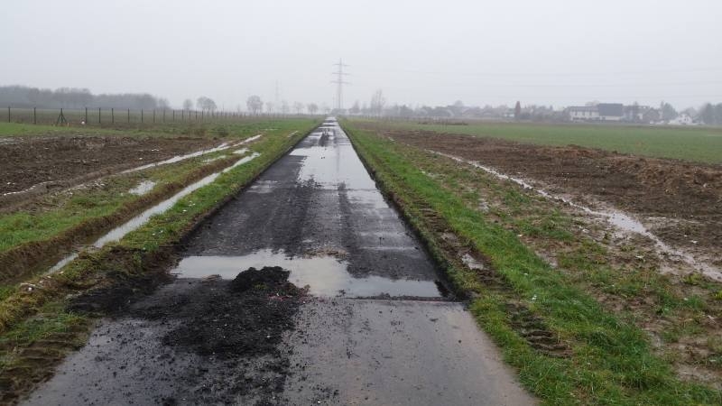 Schotter und Pfützen auf einem Weg durch Felder