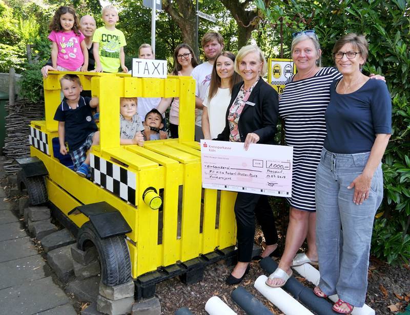 Spende für Rizzi-Projekt: v.l. stellvertretende Kita-Leiterin Ingrid Ley, Leiterin Eike Schulz, Andrea Jung (Kreissparkasse Köln) und Mitglieder des Fördervereins am „Taxi“.