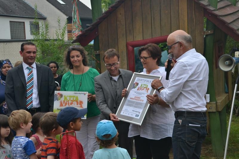 Die Übergabe des Zertifikats „gesunde Kindertagesstätte“ (v. r.) durch Helmut Thillmann (kivi e. V.) an Kita-Leiterin Ingrid Orth, in Anwesenheit von Kreis-Sozialdezernent Dieter Schmitz, Yasmin Gross (kivi e. V.) und stv. Bürgermeister Jörg Kaiser