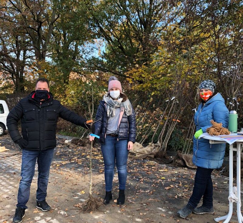 Frau Neuer (rechts) und Herr Grommes übergeben einen jugen Obstbaum an eine Bürgerin.