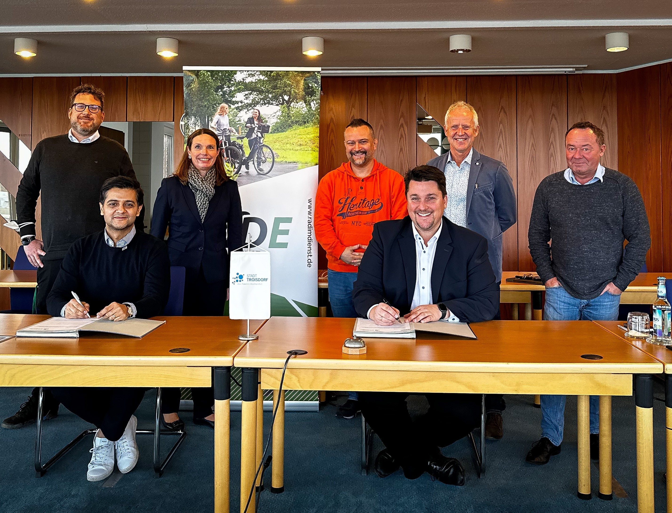 Bürgermeister Alexander Biber und Massi Naqshbandi (RadimDienst) unterzeichnen den Vertrag. Hinten v.l. Mobilitätsmanager Daniel Euler, 1. Beigeordnete Tanja Gaspers, Jan Masemann (Personalrat), Technischer Beigeordneter Walter Schaaf, Bernhard Esch (Amtsleiter Amt für Straßenbau, Erschließungsbeiträge und Verkehr)