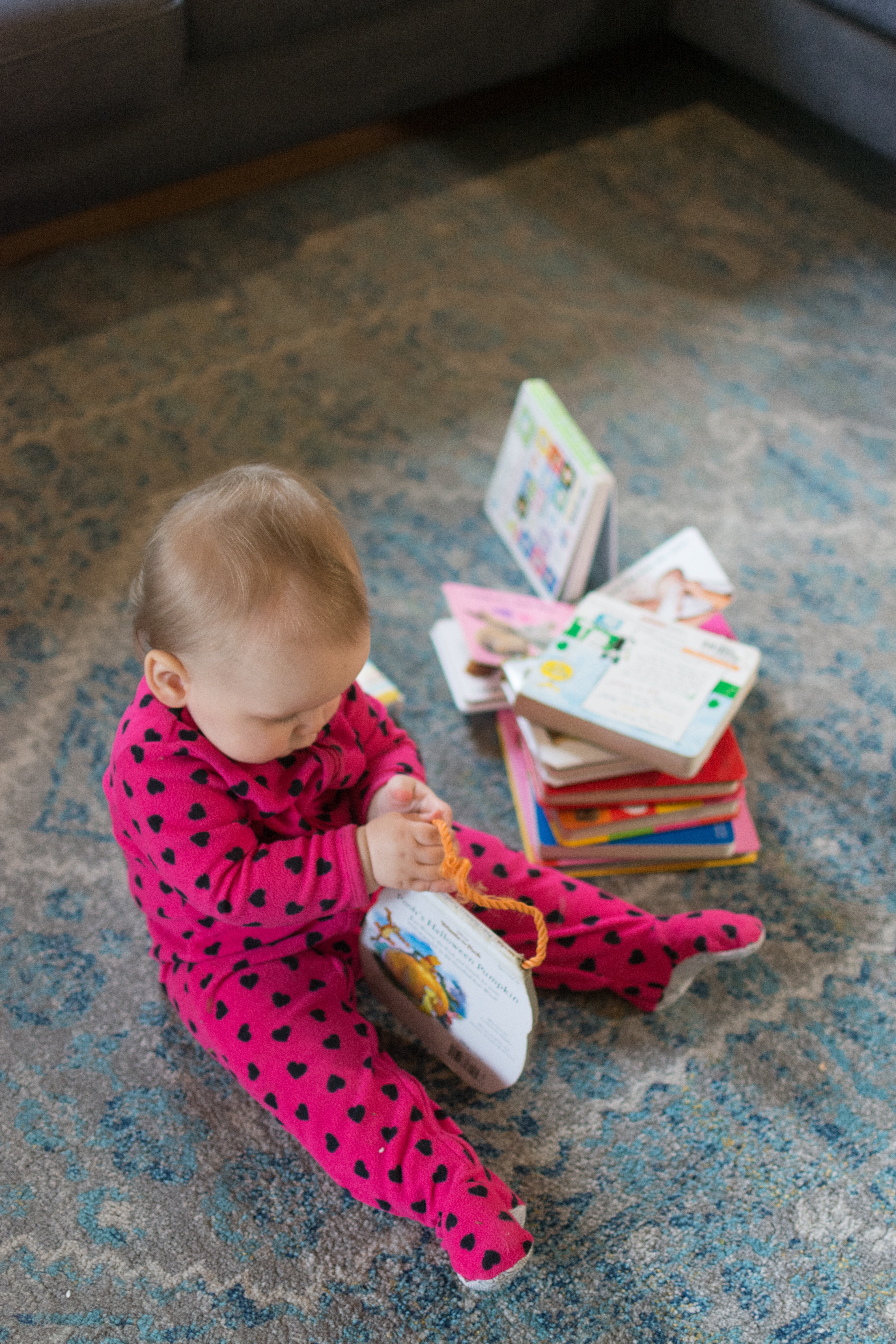 Young baby going through a pile of board books; toddler wearing