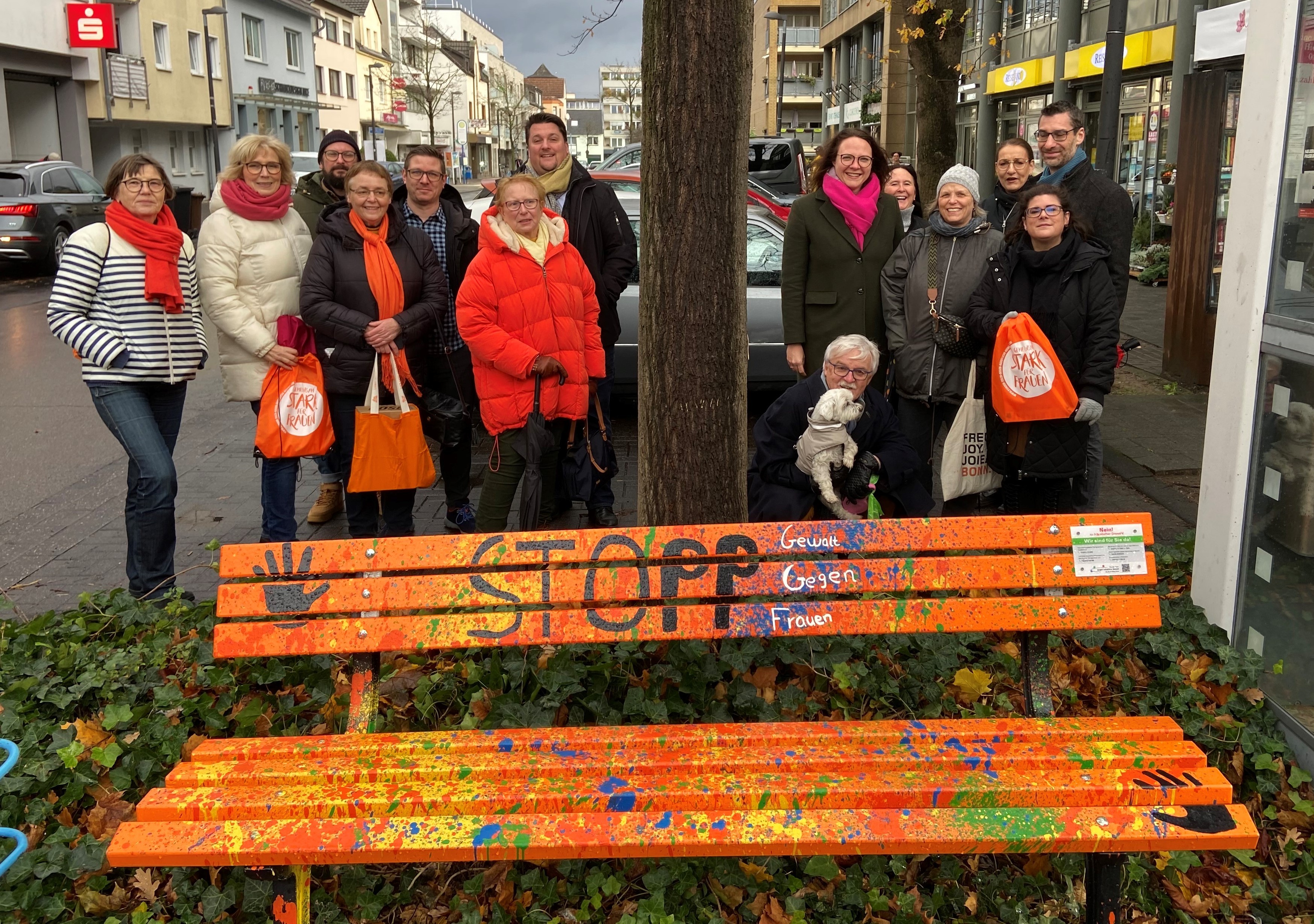 Mehrere Menschen stehen hinter einer orangefarbenen Parkbank