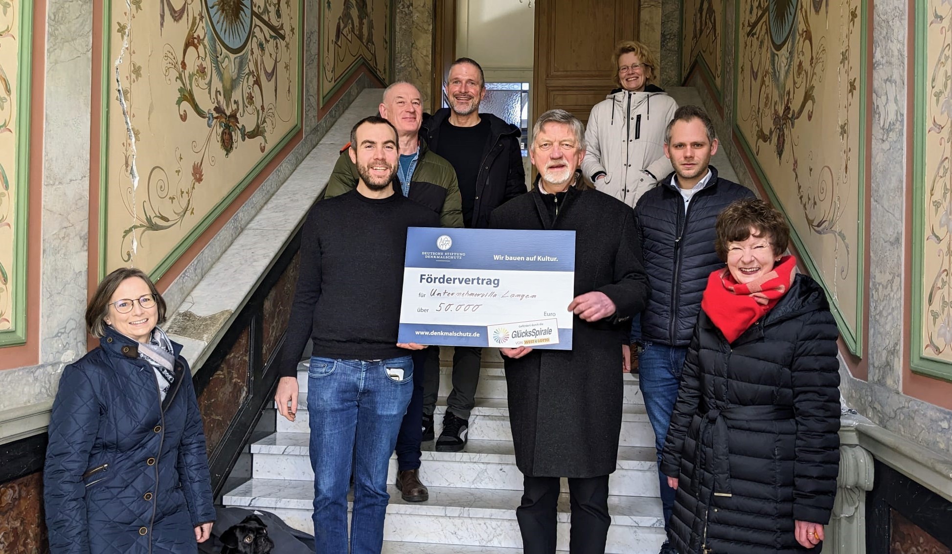 Beate von Berg (Untere Denkmalbehörde Stadt Troisdorf), Sven Riedel, Werner Braun, Andreas Dederichs (Eigentümer), Michale Wangerow (Deutsche Stiftung Denkmalschutz), Marion Grotthof (Eigentümerin), Dennis Teigelkamp (WestLotto), Angelika Müller (Deutsche Stiftung Denkmalschutz) bei der Scheckübergabe im Treppenhaus der Villa Langen.
