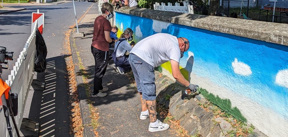 Vier Personen besprühen eine Wand mit Farbe aus der Dose