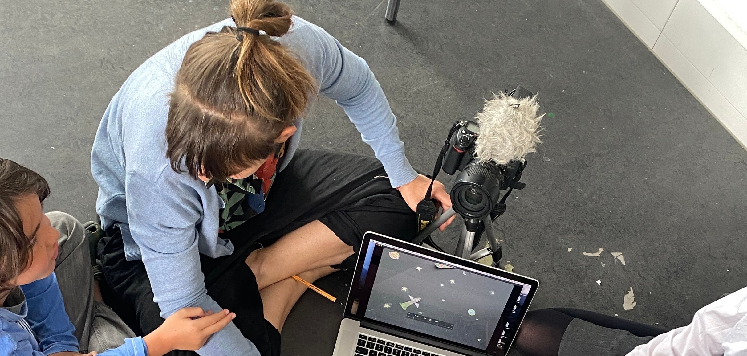 Kinder sitzen mit Leiterin auf dem Boden und besprechen etwas