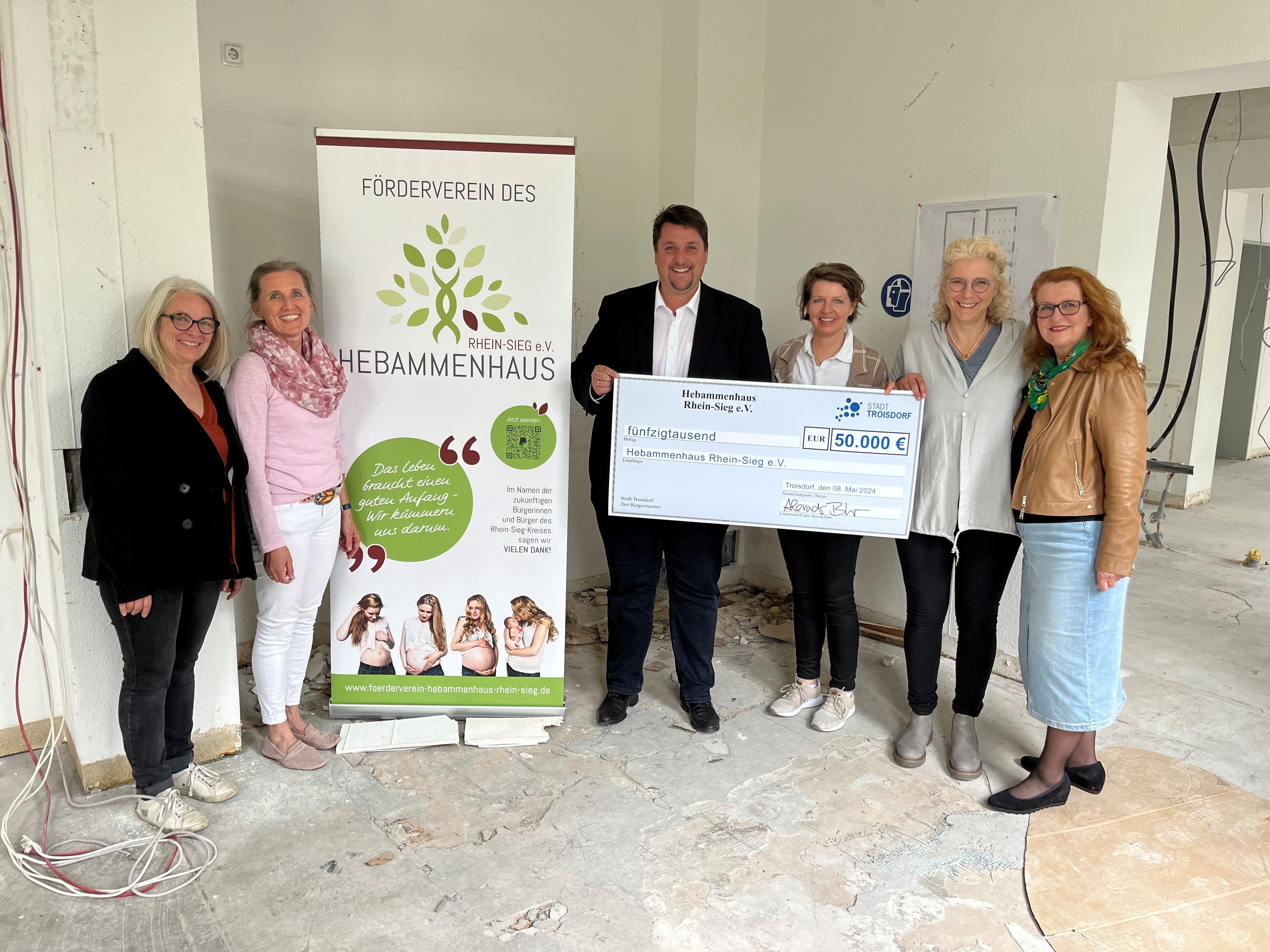 Fünf Damen erhalten einen Scheck von Bürgermeister Biber in einem unrenoviertem Raum