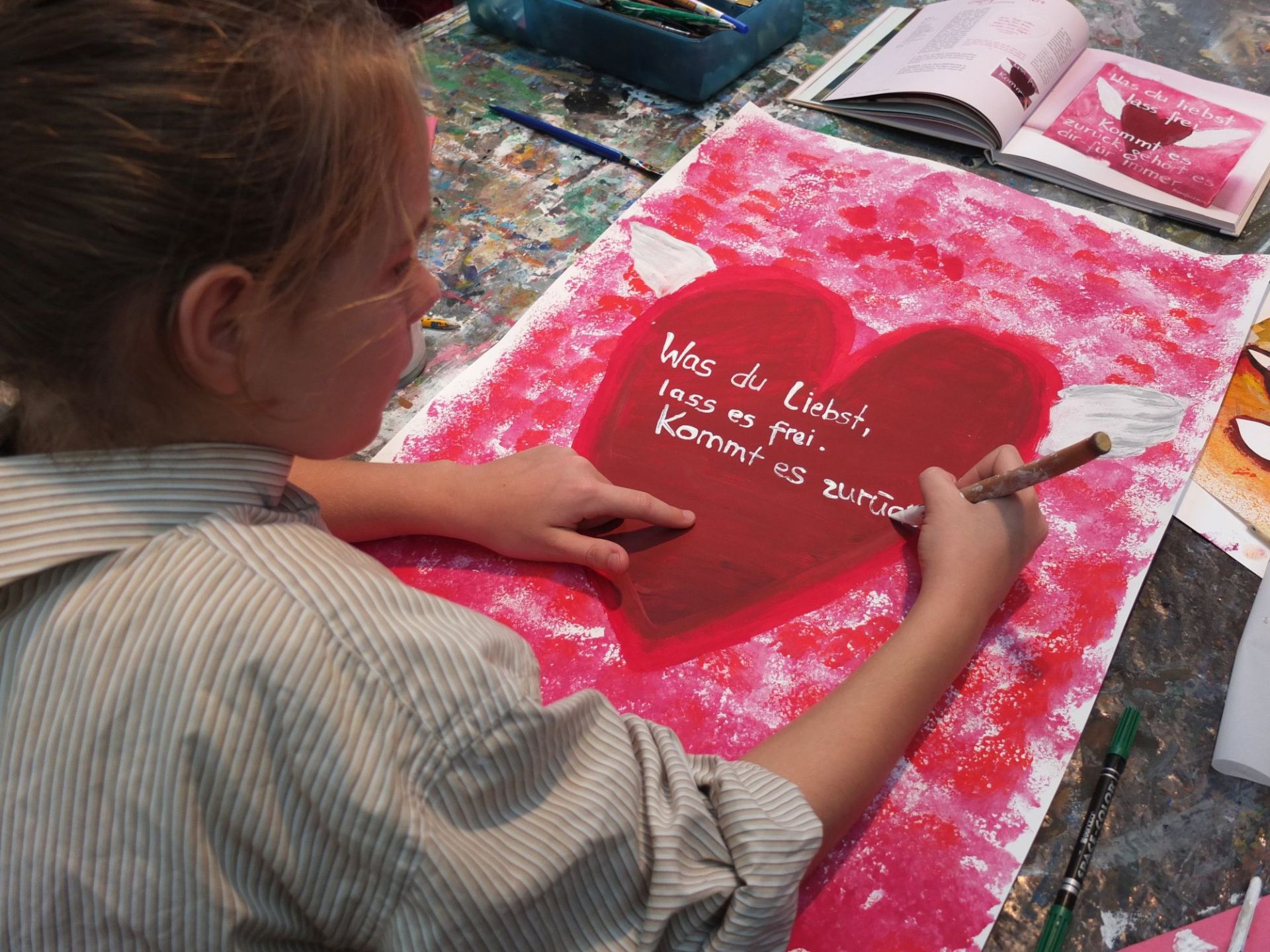 Ein Mädchen schreibt "Was du liebst, lass es frei. Kommt es zurück" in ein Herz
