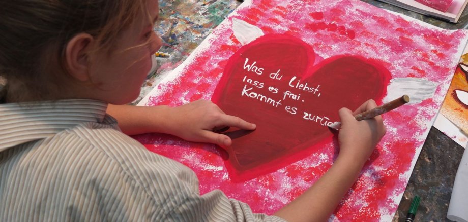 Ein Mädchen schreibt "Was du liebst, lass es frei. Kommt es zurück" in ein Herz