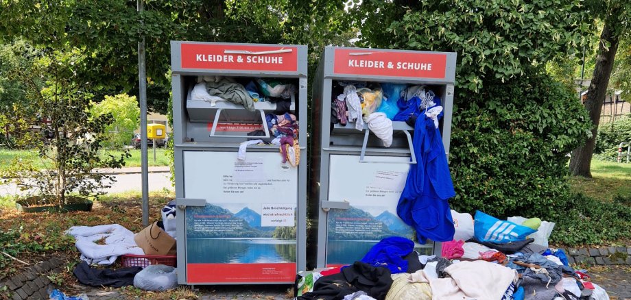 Vor den Altkleidercontainern liegen Haufen von Klamaotten