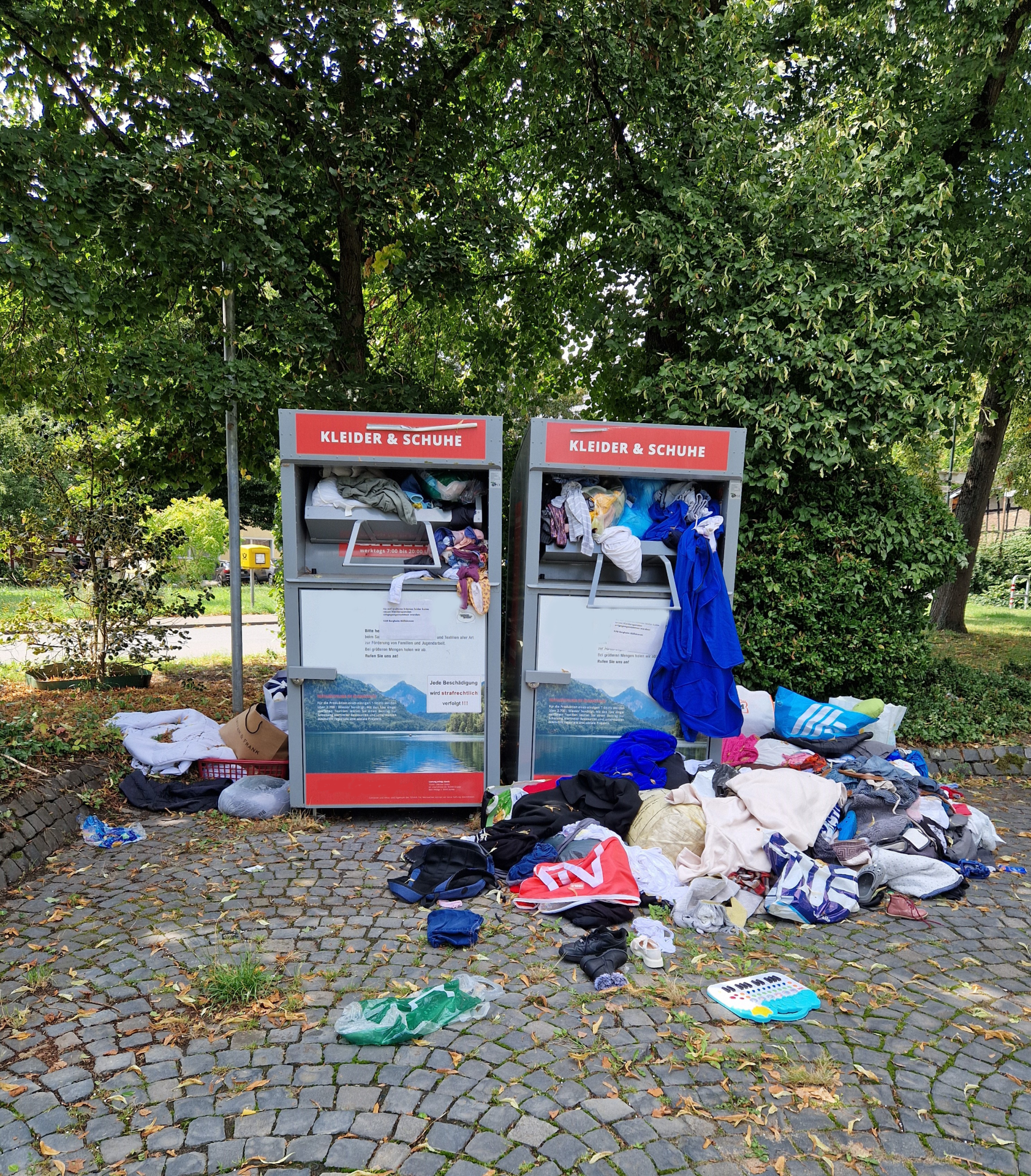 Vor den Altkleidercontainern liegen Haufen von Klamaotten