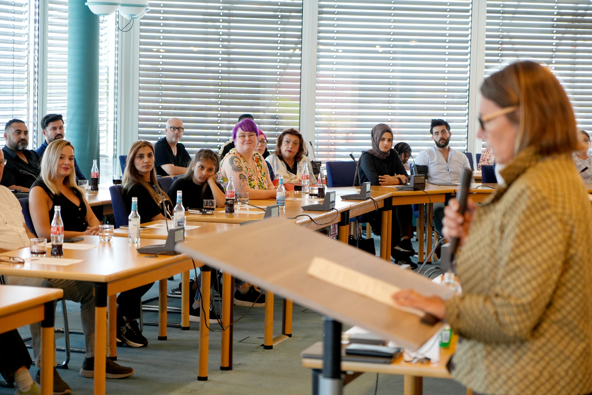 Dame spricht an Pult vor sitzenden Menschen in einem Saal