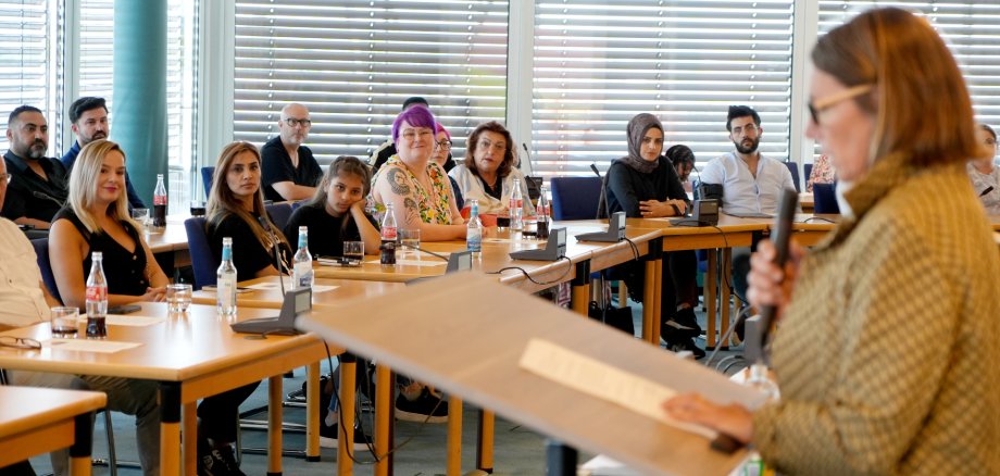 Dame spricht an Pult vor sitzenden Menschen in einem Saal