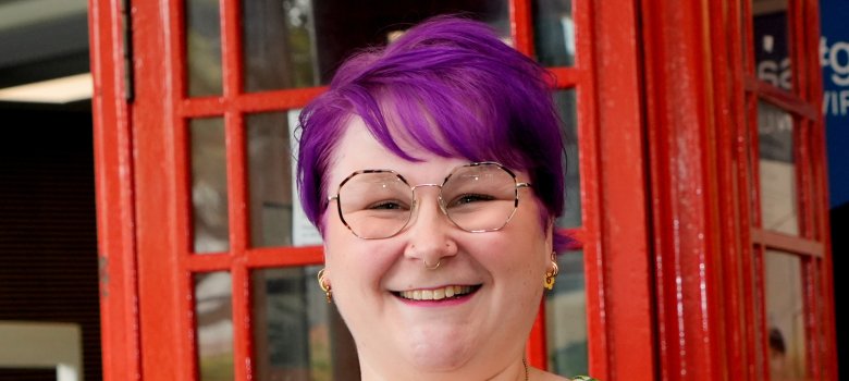 Junge Frau mit Urkunde vor roter, britischer Telefonzelle