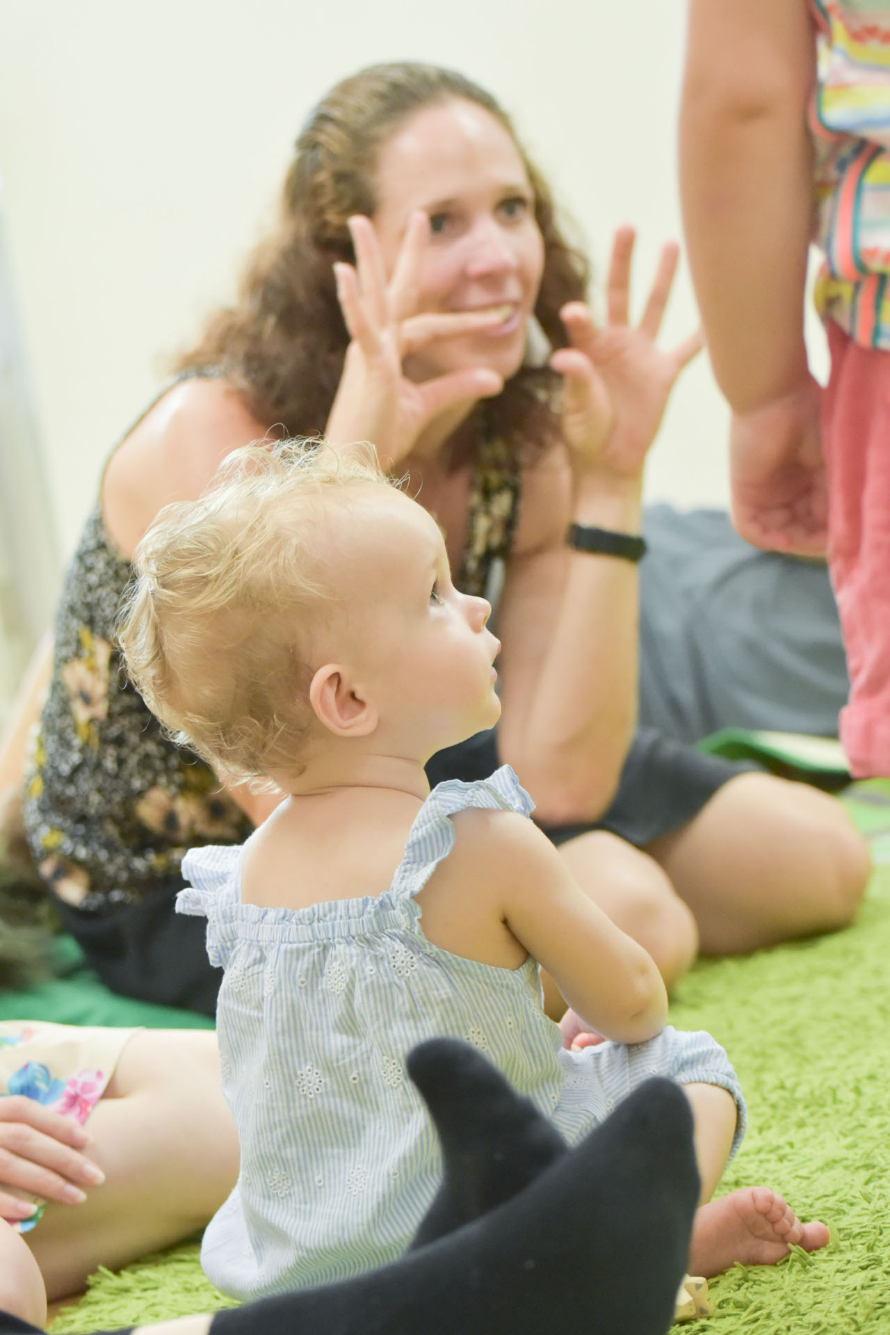 Ein Kleinkind und im Hintergrund eine Frau, die miit den Händen etwas zeigt