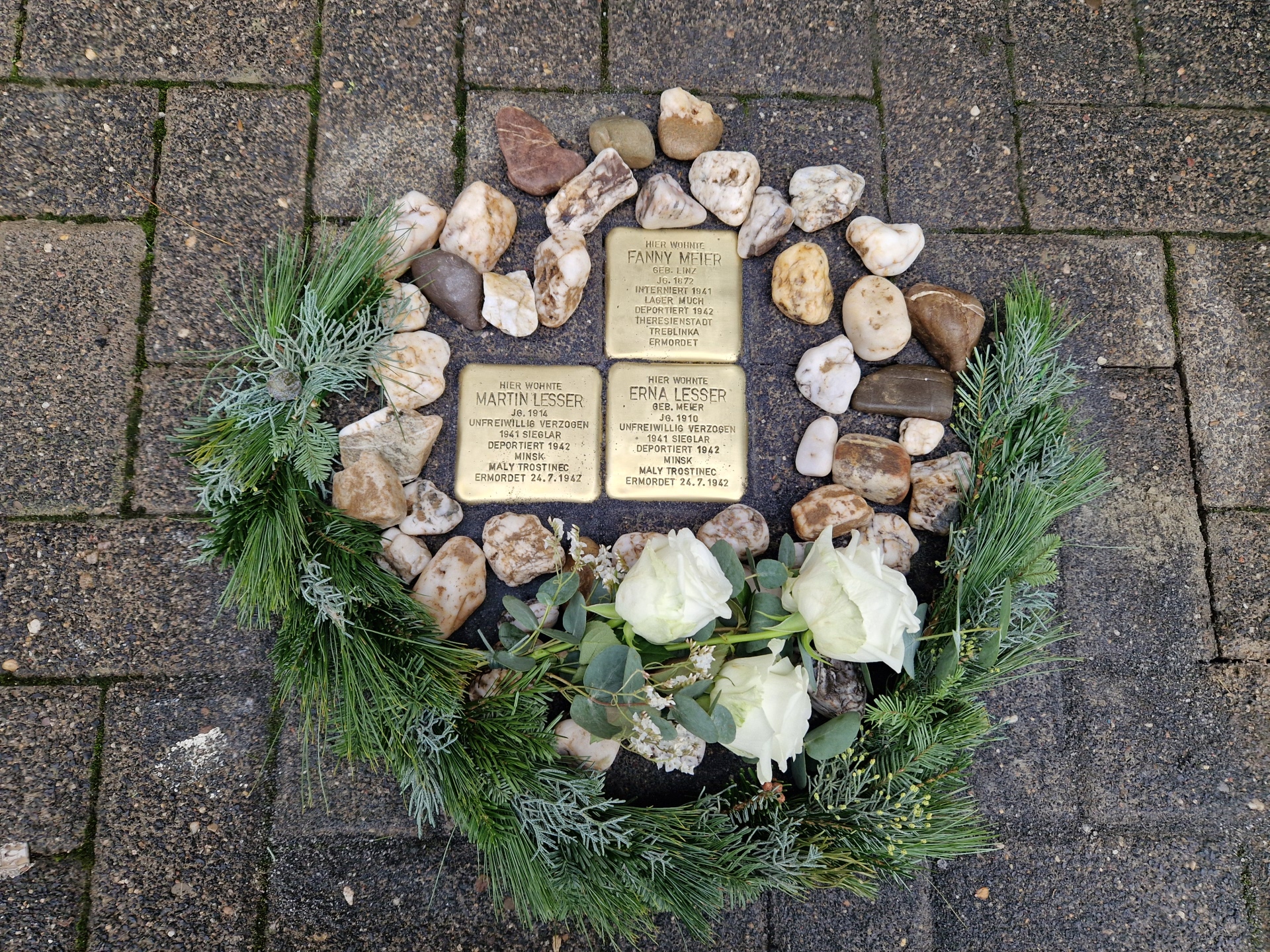 Die drei Stolpersteine, dekoriert mit Steinen und einem Tannenkranz