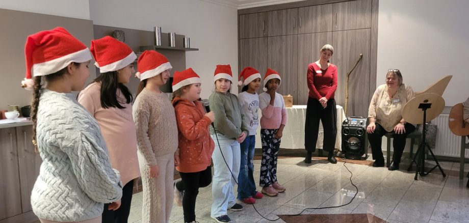 Eine Gruppe von Kindern, ausgestattet mit Weihnachtsmützen singen in einer kleinen Gruppe