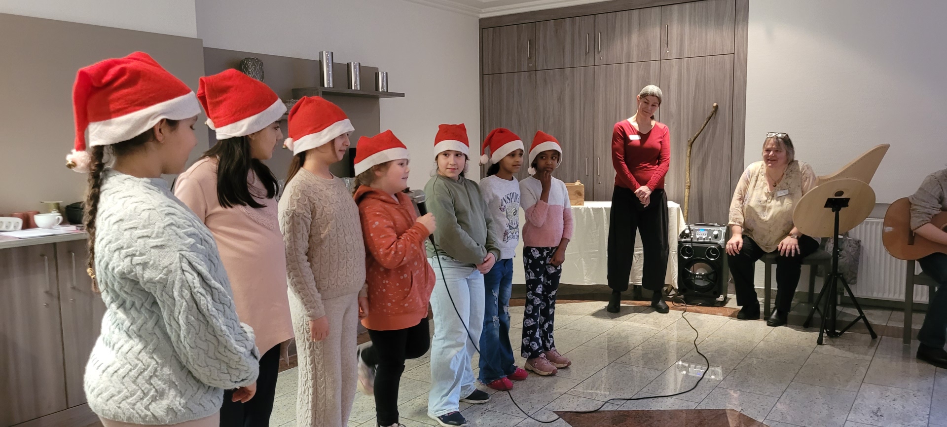 Eine Gruppe von Kindern, ausgestattet mit Weihnachtsmützen singen in einer kleinen Gruppe