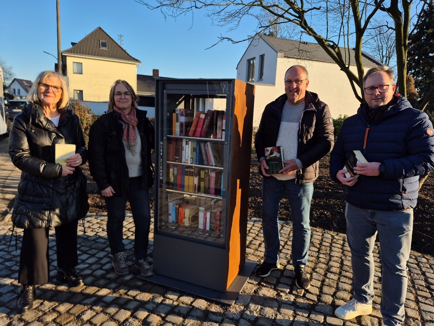 Freuen sich über die die kleine Bibliothek an der neuen Grünflache:  v.l. Bücherschrank-Patin Hanne Brohl, Kerstin Kuffner vom Amt für Grünplanung, Ortsvorsteher Wolfgang Weithe-Berchtold und der Vorsitzende des Ortsrings Müllekoven Frank Peukert