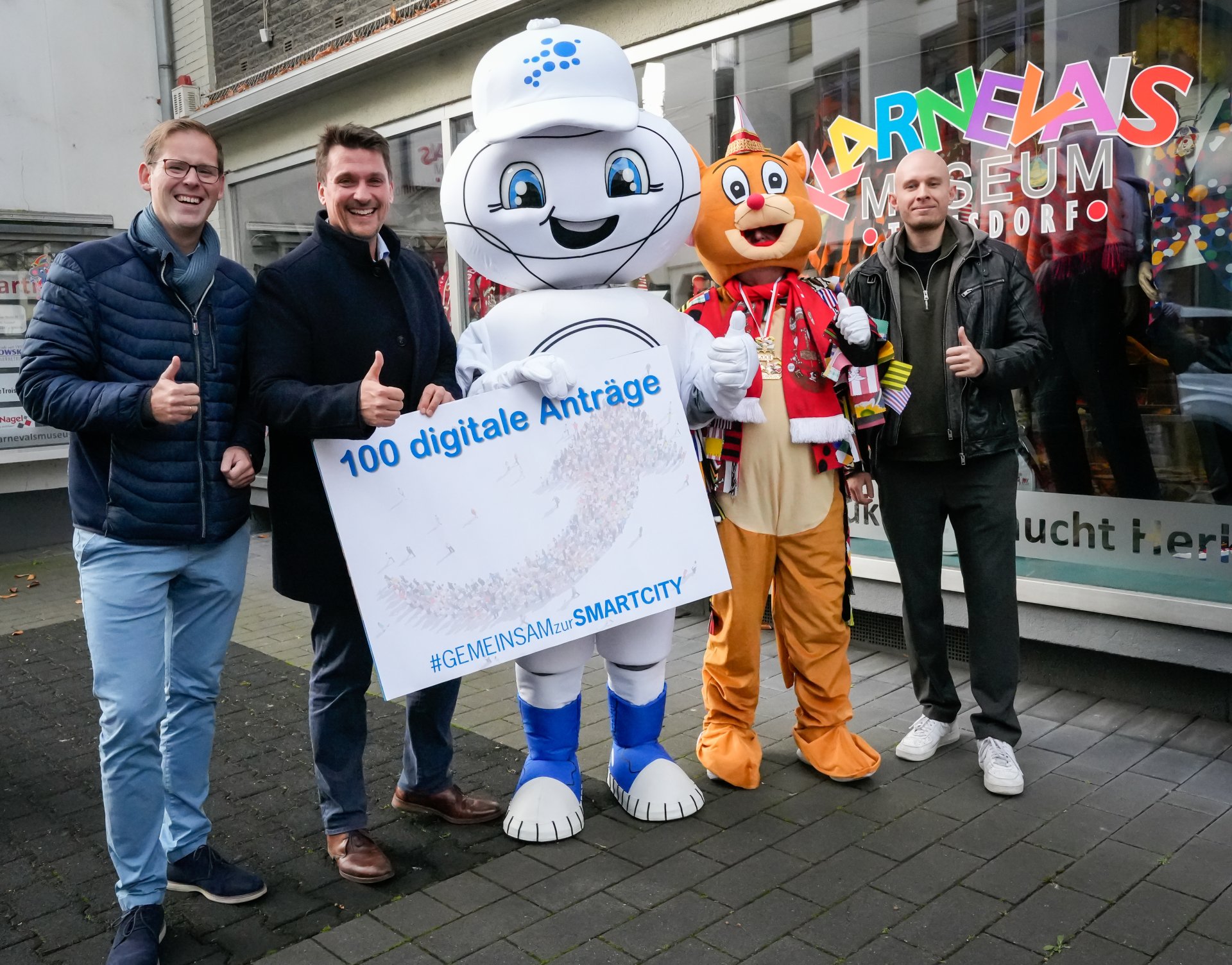 Gemeinsam wird der 100. digitale Antrag gefeiert v.l Fabian Wagner, Leiter der Stabsstelle Digitalisierung, Bürgermeister Alexander Biber, Maskottchen Smarta, die Maus des Karnevalsmuseums und Sebastian Glees, Projektleiter Digitales Rathaus der Stadt Troisdorf.