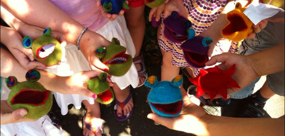 Zu sehen sind Kinder mit bunten Filz-Fröschen in der Hand