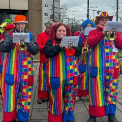 Als Clowns verkleidete spielen auf Blasinstrumenten.