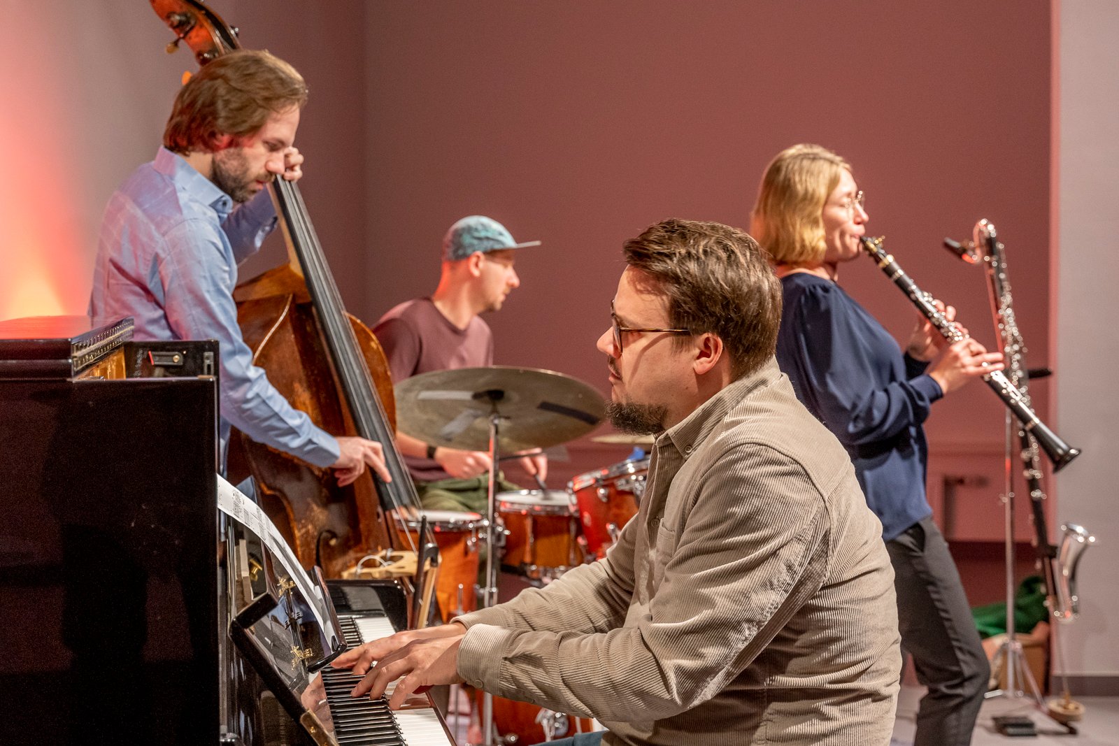 Ein Mann spielt Klavier im Vordergrund. Im Hintergrund werden andere Instrumente gespielt