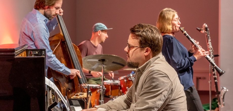 Ein Mann spielt Klavier im Vordergrund. Im Hintergrund werden andere Instrumente gespielt