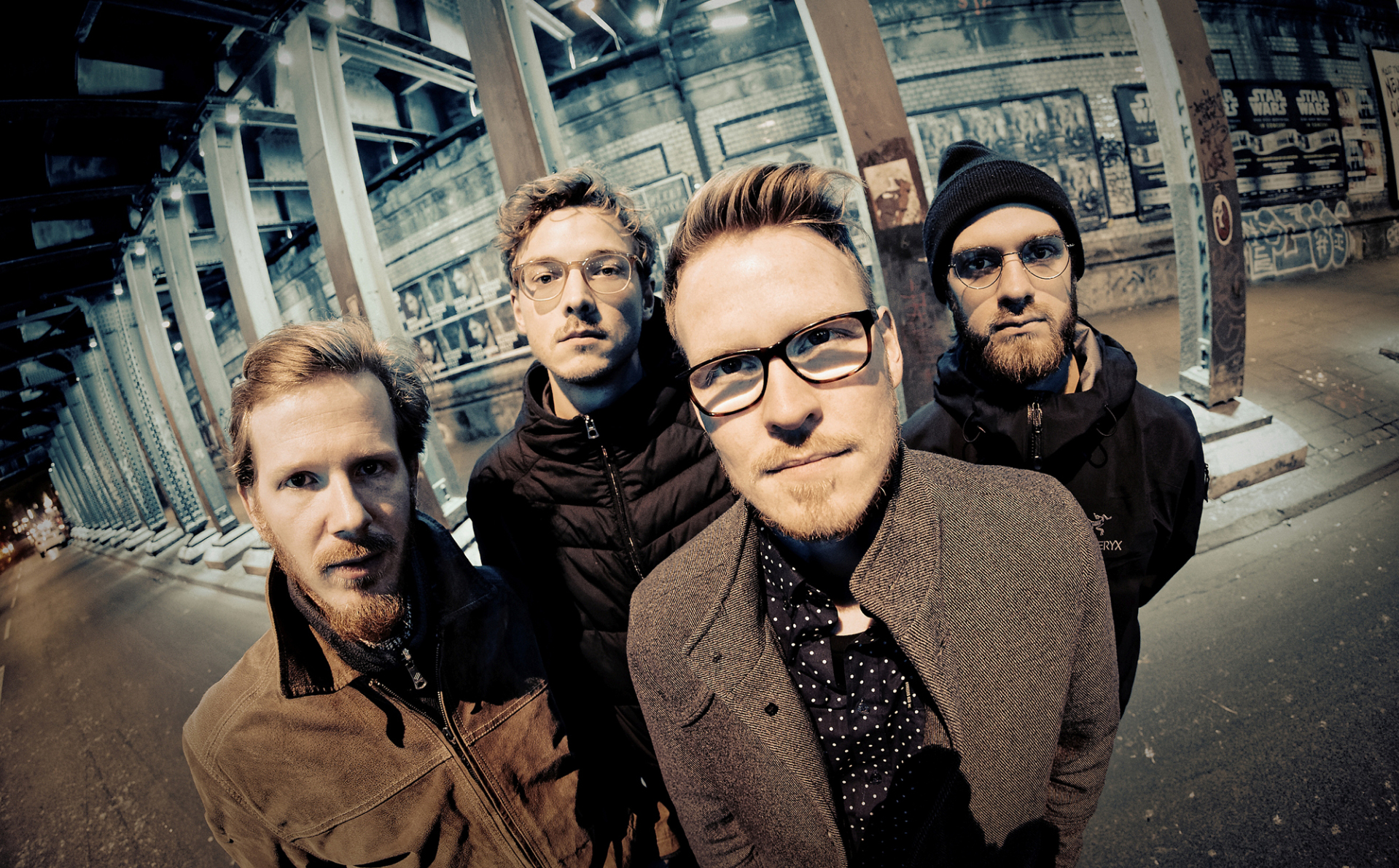 Vier Männer in Graffiti-Halle, dunkle Jacken, einer in hellbraun, Band: Schmid's Huhn.