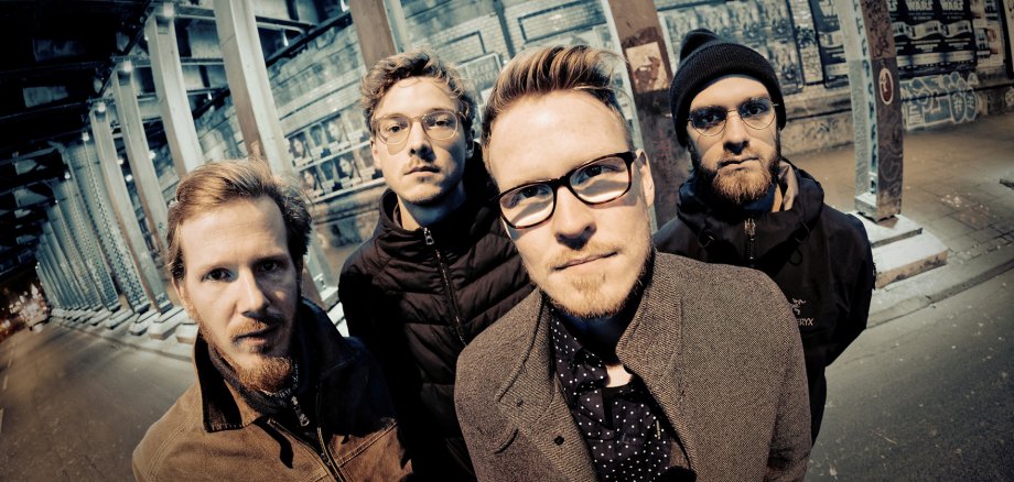 Vier Männer in Graffiti-Halle, dunkle Jacken, einer in hellbraun, Band: Schmid's Huhn.