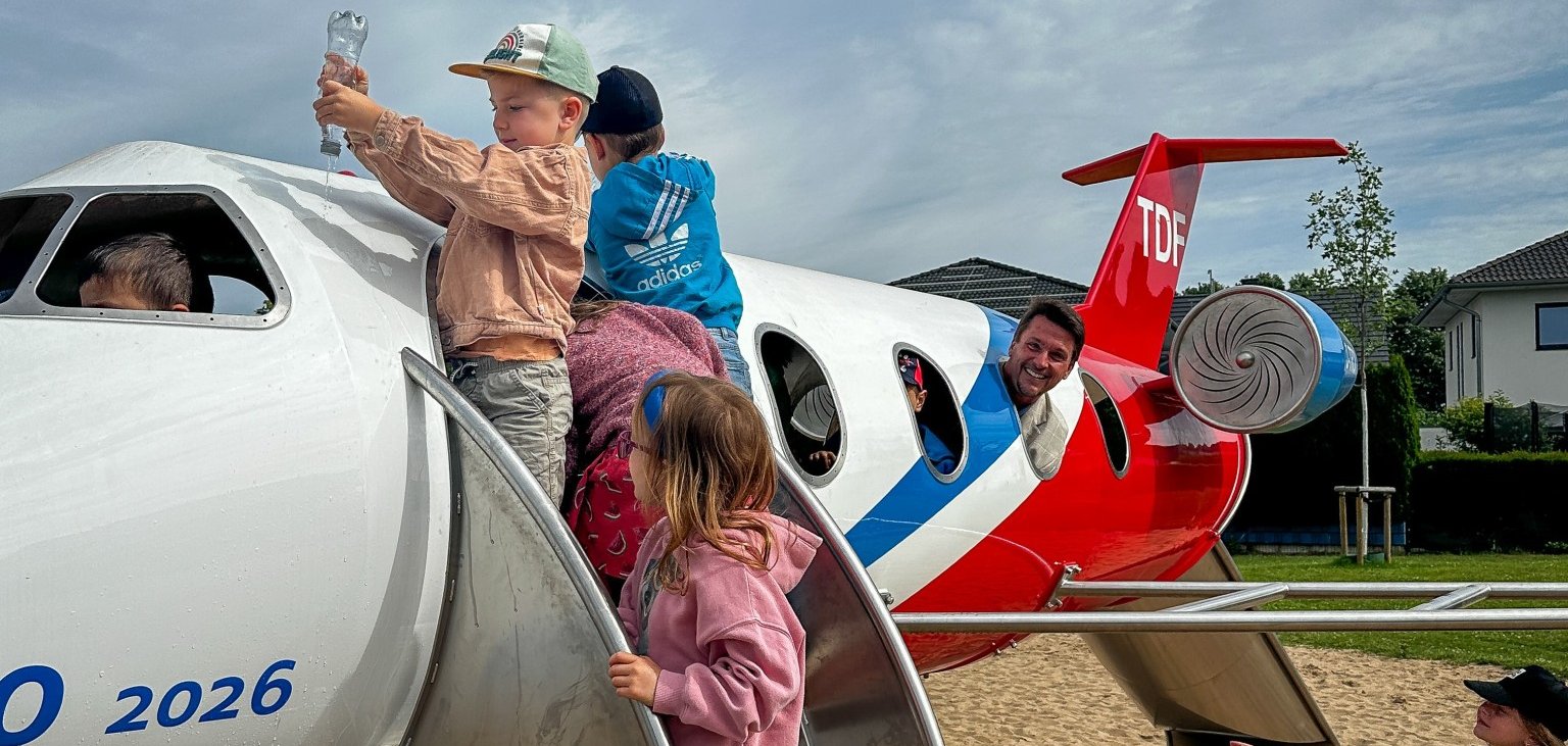 Bürgermeister Alexander Biber schaut aus dem Fenster des Flugzeugs, während Kinder im und am Flugzeug spielen.