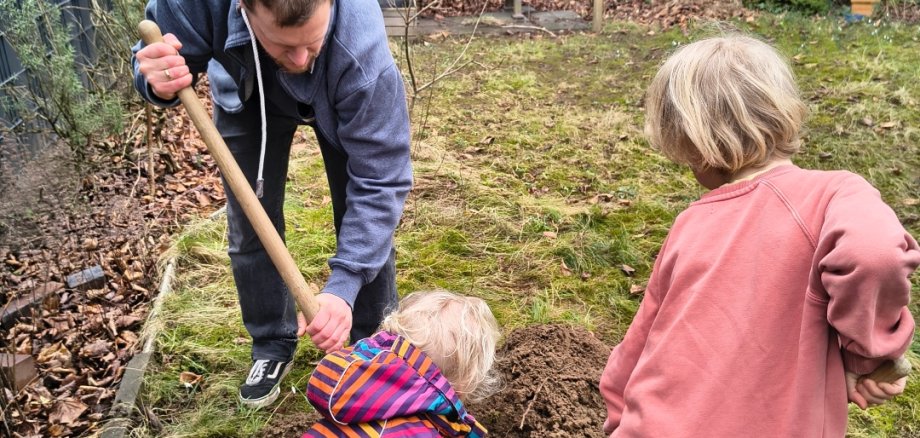 Ein Mann pflanzt mit zwei Kindern einen Baum