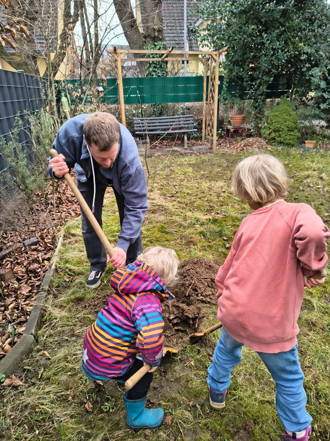 Ein Mann pflanzt mit zwei Kindern einen Baum