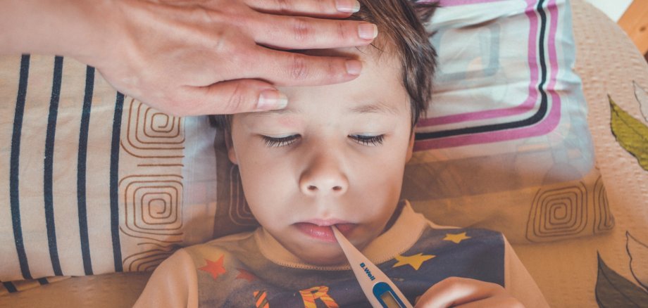 Kranker Junge im Bett mit Fieberthermometer Kranker Junge im Bett mit Fieberthermometer