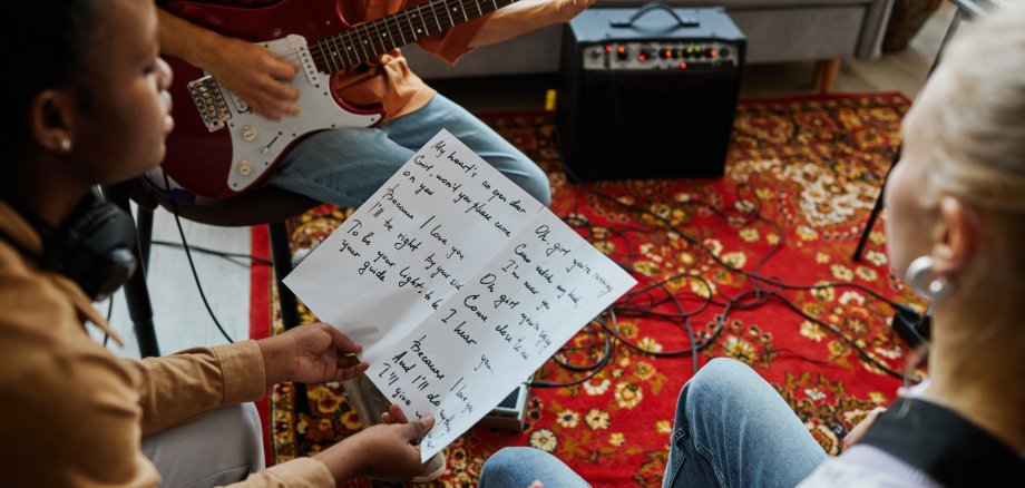 Songwriting Nahaufnahme einer jungen Frau, die gemeinsam mit einer Musikband Songs schreibt und ein Blatt mit Liedtexten hält