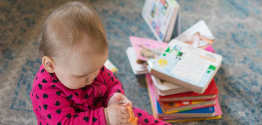 Young baby going through a pile of board books; toddler wearing