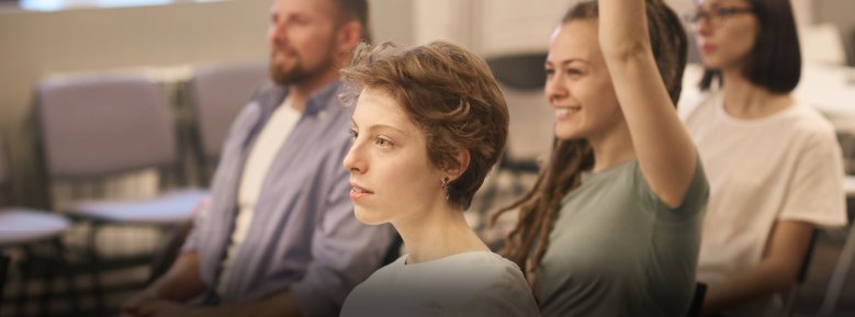 Drei Personen in einem Raum. Eine Frau meldet sich